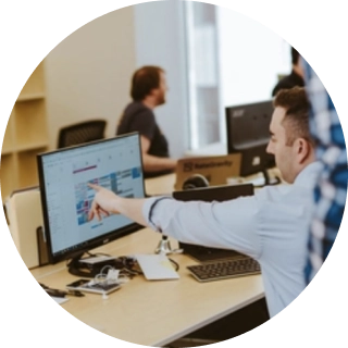 Own Up Co-founder Mike Tassone seated at a desk, pointing to a computer monitor while a colleague observes