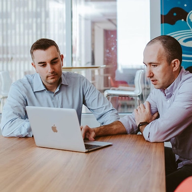 two men sitting at table with laptop