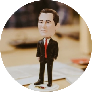 A bobblehead figurine of a standing business person wearing a black suit and red tie